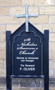 Blue painted sign with lettering, a white cross above the writing, fixed to upright posts.