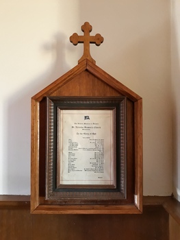 The document contains a list of text. It is behind glass in a timber frame, the top edge is an inverted V with a cross