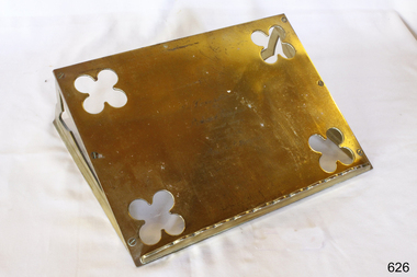 Brass bible rest has ledge across bottom and sits at an angle on the flat surface. It has decorative cutouts.