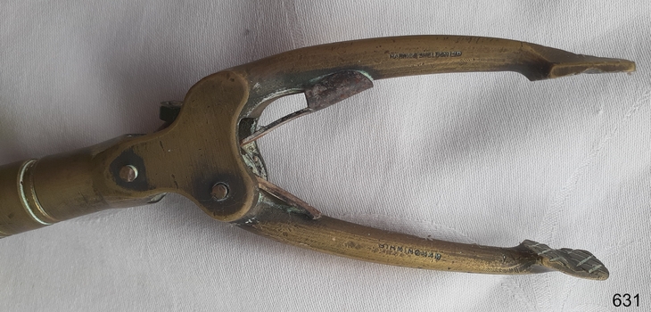 Metal mechanism has two arms and has inscriptions. Flat pads on the end of the arms have cross hatching lines.