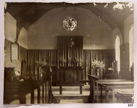 Sepia photograph showing inside a religious building with altar, pews, lectern, vases, candlestick holders etc.