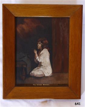 Framed painting of a child clothed in white, kneeling in prayer. It has an inscription 