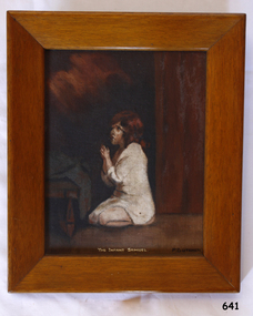 Framed painting of a child clothed in white, kneeling in prayer. It has an inscription 