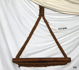 Plank of wood with rope threaded through holes in each end and spliced together underneath. Ropes are joined at the top with rope work.