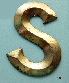 Gold coloured letter 'S', three dimensional, with nicks and scratches