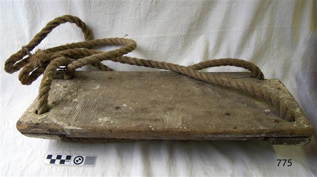 Plank of wood as seat hung from looped rope threaded through four drilled holes in corners of plank