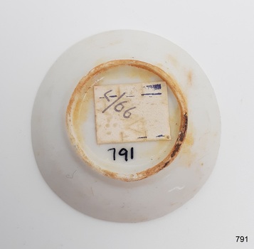 Saucer has brown stains around the raised part of base, a white sticker with text and a number