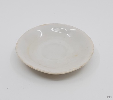 White ceramic toy saucer, slightly oval, glazed, uneven sruface