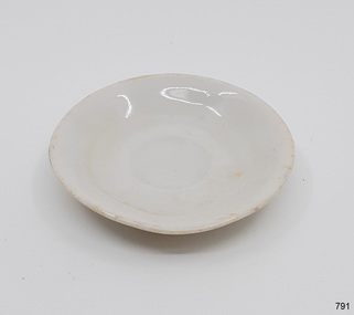 White ceramic toy saucer, slightly oval, glazed, uneven sruface