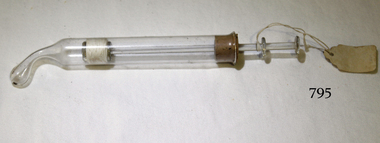 A glass syringe with curved end. The plunger at the other end of the syringe is inserted through a cork.