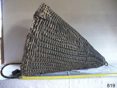 Woven cane cone, painted black, with a vertical metal rod through the centre.