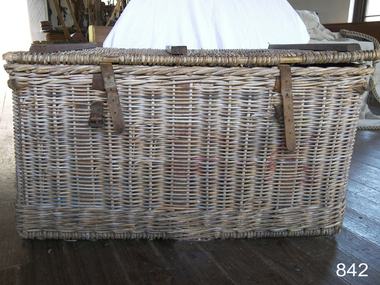 Front of basket with two leather straps and buckles for fastening the woven fitted lid on top. The wooden reinforcing lengths on the lid are also visible.