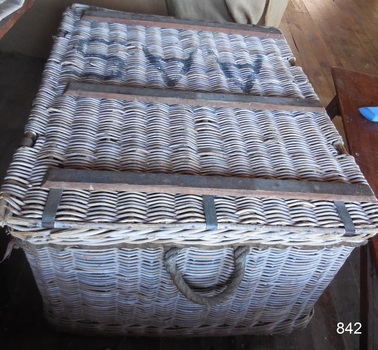 Attached to the side of the basket is a strong rope handle, There is another one on the other side. The metal straps reinforcing the lid are clearly visible.