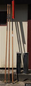 Three rocket poles leaning on wall, one has rocket fitted to the top. Two rocket head toting boxes stand beside the poles.