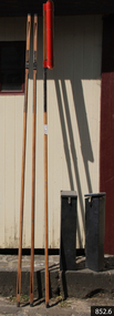 Three rocket poles leaning on wall, one has rocket fitted to the top. Two rocket head toting boxes stand beside the poles.