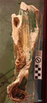 Long piece of ceramic work with edges that have been broken. Paint fragments of brown, black, green 