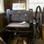 Tall treadle machine with a flat bed, a wheel on top and a wheel and larg gears on the side