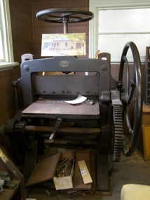Tall treadle machine with a flat bed, a wheel on top and a wheel and larg gears on the side