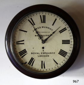 Round timber encased clock has Roman numerals, two hands, text and a key hold.