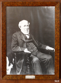 Black and white portrait, main in suit, seated in wooden arm chair