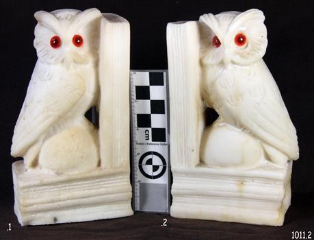 White owls with red eyes, facing each other, heads turned towards viewer. 
