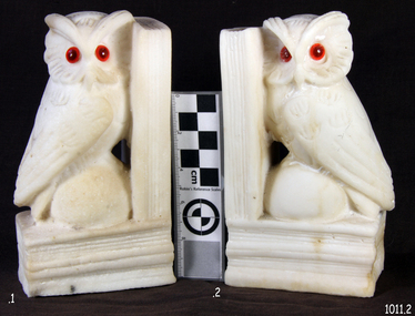 White owls with red eyes, facing each other, heads turned towards viewer. 