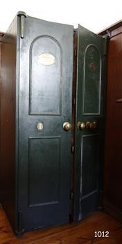 Green painted iron safe had double doors, each slightly open. There is an oval plaque on the top section of each door.