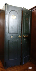 Green painted iron safe had double doors, each slightly open. There is an oval plaque on the top section of each door.