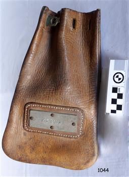 Leather bag, rounded bottom corners, holes in top for drawing together, stitched frame around metal nameplate