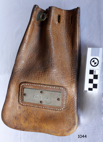 Leather bag, rounded bottom corners, holes in top for drawing together, stitched frame around metal nameplate
