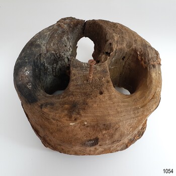 Round timber block with three holes. There is a nail in the centre.