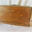 The wooden case is clipped onto the base of the machine, leaving the bottom of the base still visible. It has a folding metal carrying handle on the top. 
