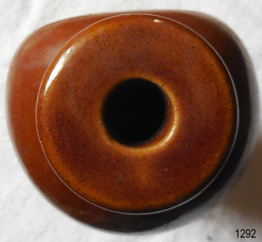 The uneven gritty texture and colour of the clay shows through the brown glaze of the mouth and shoulders. The photo shows that the flat side of the bottle is about a sixth of the side of the bottle.