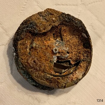 Front of fragile pocket watch with  encrustations and parts broken away