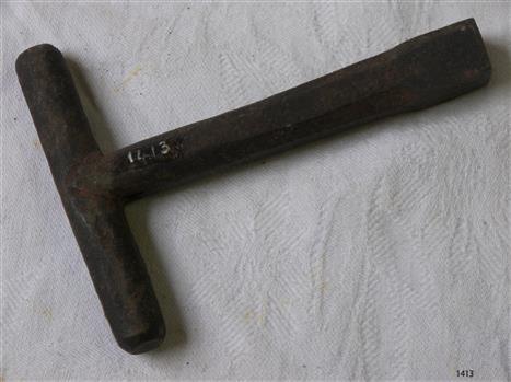 Metal key is T shaped with a round handle at the top of a hexagonal shaped shaft