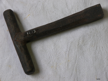 Metal key is T shaped with a round handle at the top of a hexagonal shaped shaft