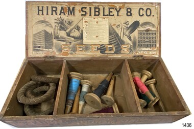 Wooden box has assorted items in its three compartments. Printing under the lid about seeds and company