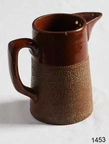 Two tone brown stoneware jug with handle. Lighter brown e stippled lower part, darker brown plain upper part.