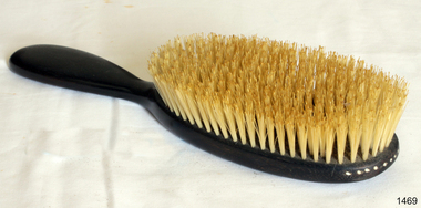 Brown ebony handle and oval -shaped back with bristles.