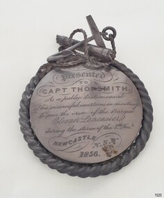Round silver medal with inscription. Robe border around edges, anchor and rope decoration on top