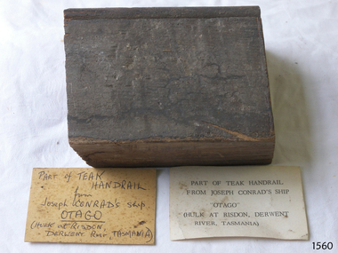 Small block of dark coloured timber with a groove along one edge. Two card labels are included.