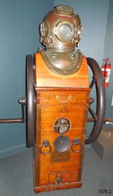 Diving compressor has manual crank handles at sides, and helmet attached