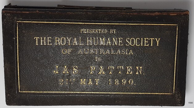 Dark coloured lid has gold embossing; rectangular frame with six rows of text explaining contents