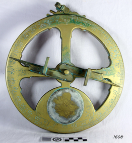 Gold-coloured disc shape with cup-outs, an indicator arrow, and a ring on the top.