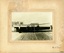 Black and white photograph mounted on cream card with inscription lower right; five men in front of a boat.