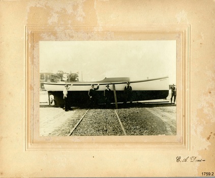 Black and white photograph mounted on cream card with inscription lower right; five men in front of a boat.