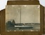 Sepia photograph mounted on card, stamped lower right. Seven men standing behind a small sailing boat.