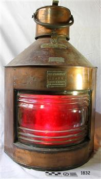 Brass and glass lamp with red coloured lens and brass plates with inscriptions