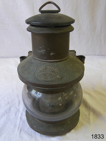 Round metal lamp with glass lens, hanging hook and maker's plate