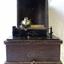 Phonograph with lid off, crank handle on bench in front of machine.
